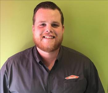 man with brown hair and red beard wearing a gray shirt in front of a green wall 