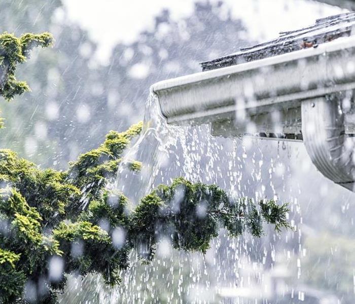 Rain storm water is overflowing off a roof - streaming, rushing and splashing out over the overhanging eaves trough aluminum 