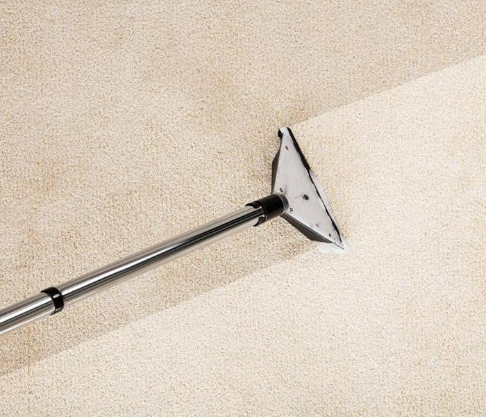 A close-up of a carpet cleaning machine cleaning a dirty beige carpet